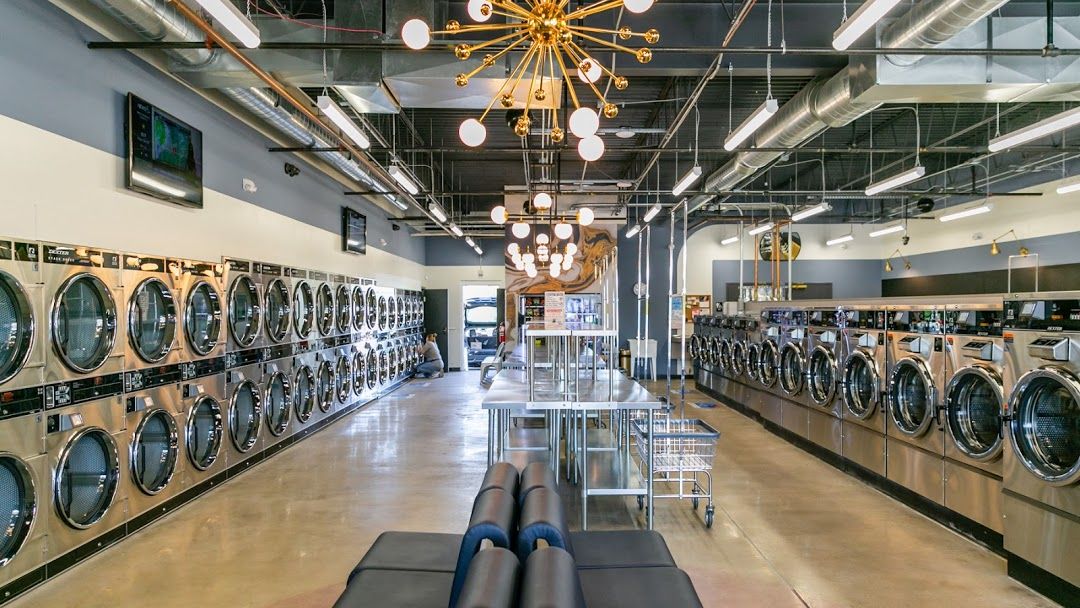 Modern laundromat interior with rows of stainless steel washing machines and dryers